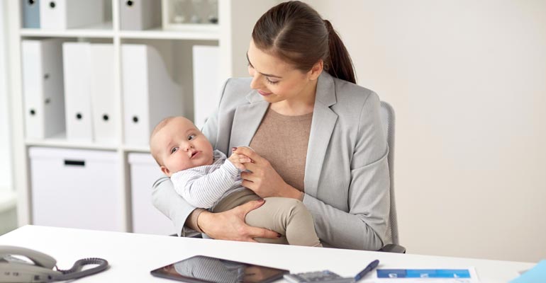 signs you're facing retaliation for taking fmla leave woman holding baby at work sitting at desk