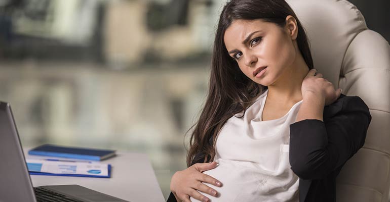 stressed and tired pregnant woman sitting at her desk at work