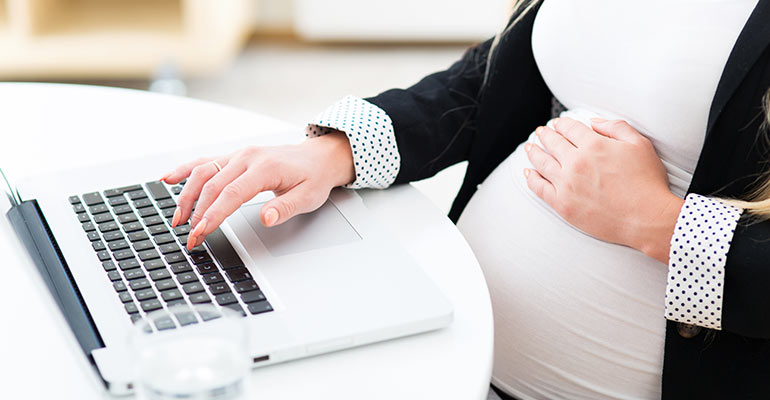 pregnant woman at desk typing and holding stomach