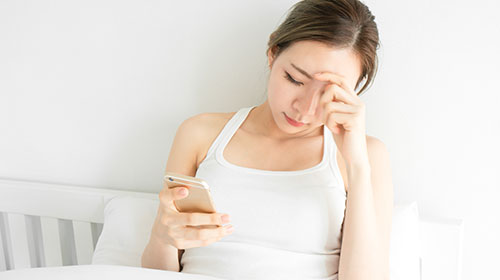woman holding phone and have a headache in white bedroom after wake up