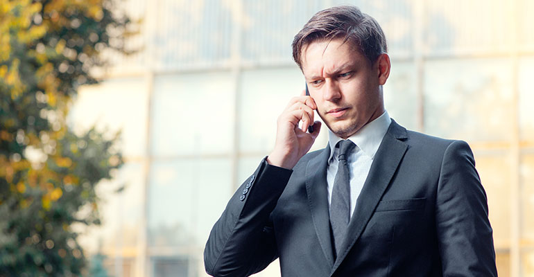 businessman in suit and tie talking on the mobile phone while standing outdoors with office building in the background