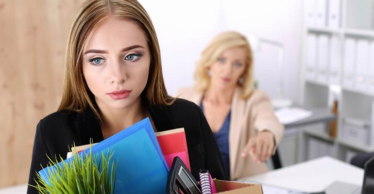 Woman leaving office with box of belonging and being asked to leave by female employee