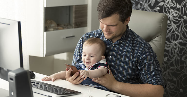 Man holding baby in lap at desk looking at smartphone