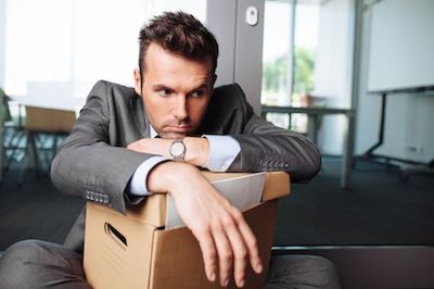 man seated holding box of belongings after being fired from job