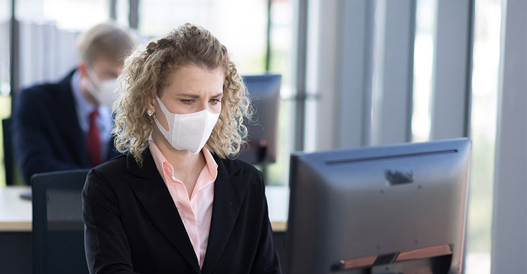 Woman working in the office on the computer with a mask on