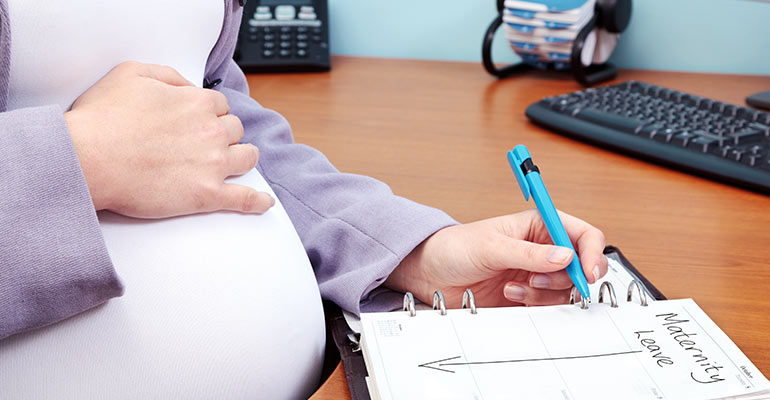 pregnant woman sitting at desk looking at calendar and preparing for maternity leave