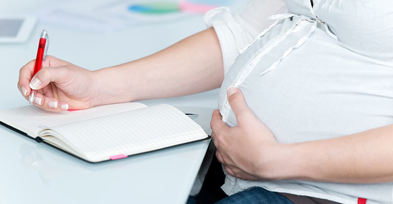 pregnant woman sitting at desk holding stomach and writing in journal