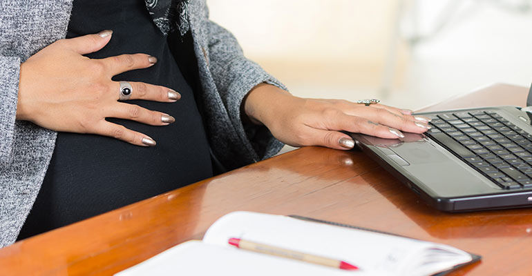 pregnant woman holds stomach while at desk