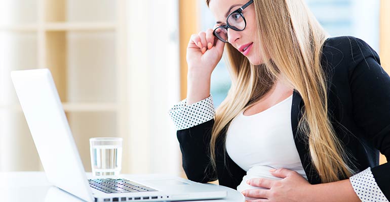 pregnant woman sitting at desk with hand on glasses and stomach