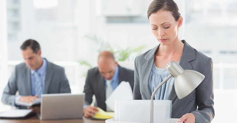woman carrying box out of office with male employees in background