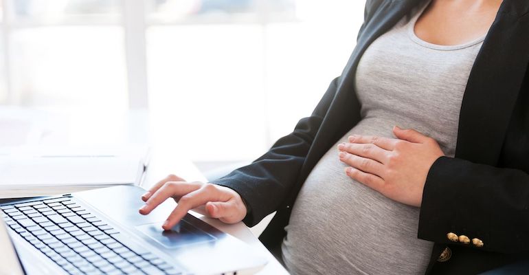 Woman holding her pregnant belly while working