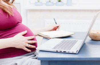 Woman holding her pregnant stomach while working on the laptop