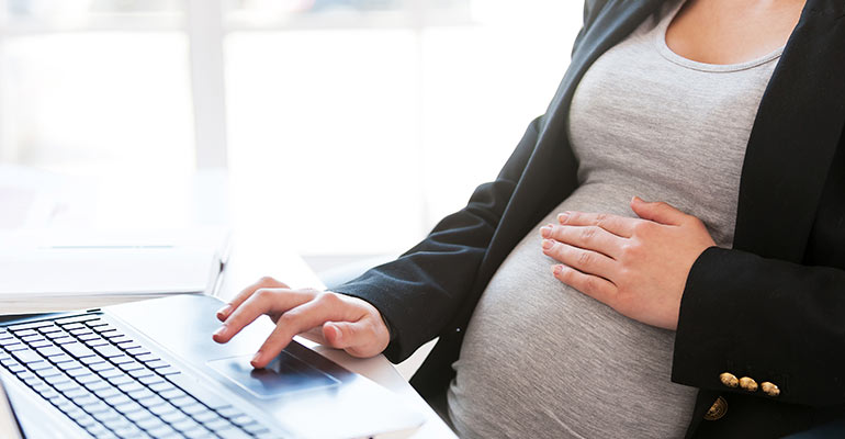 pregnant woman sits at desk typing
