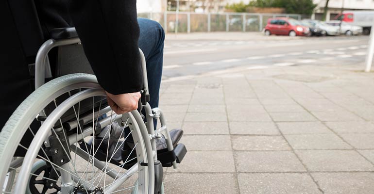 Man in wheelchair going down city walkway