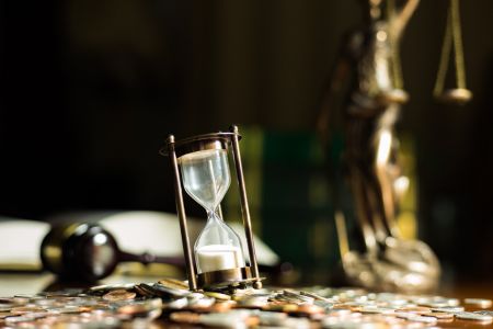 Hourglass resting on top of coins next to a gavel