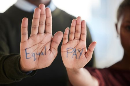 Two people holding up hands that together say "Equal Pay"