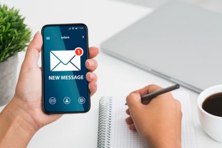 Person at desk with smartphone with notifications and taking notes on notepad.