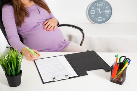 pregnant worker completing paperwork while seated at an office workstation.