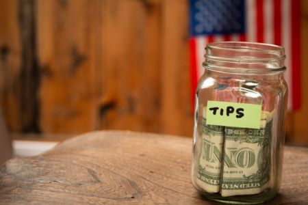 tip jar with cash representing employee wages and earned gratuities