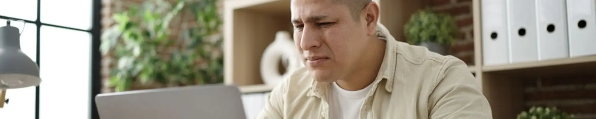 Hispanic professional looking concerned while working on a laptop in an office