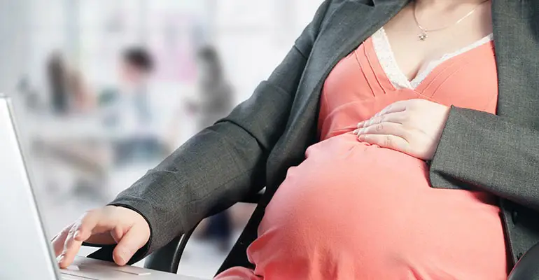 pregnant woman sitting at her desk working with one hand on her stomach