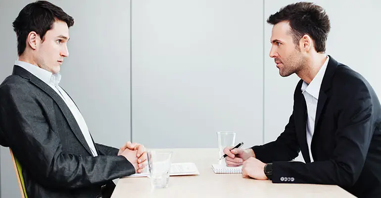aggressive man stairs at worried man at desk