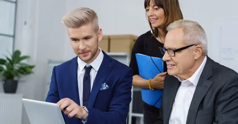 older man sitting with younger employee looking at tablet