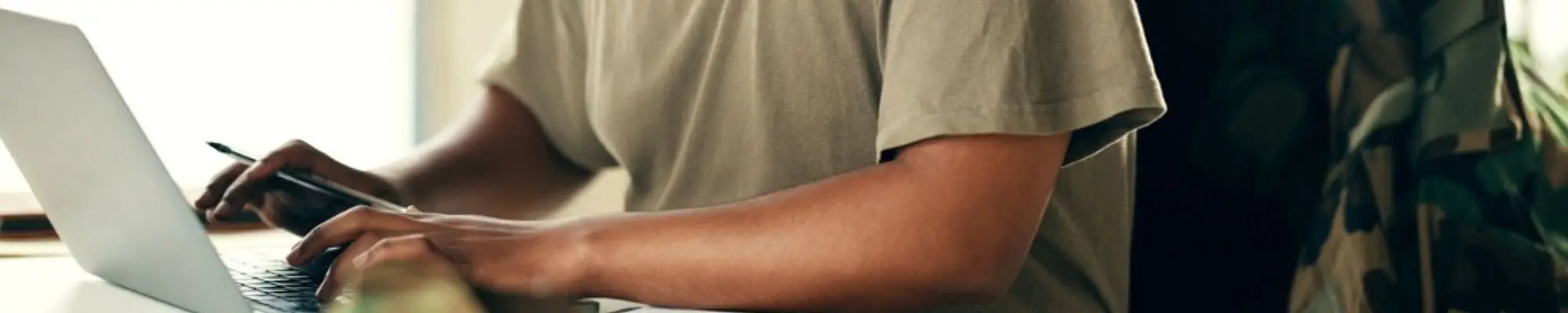 Military service member working on a laptop with his uniform jacket nearby