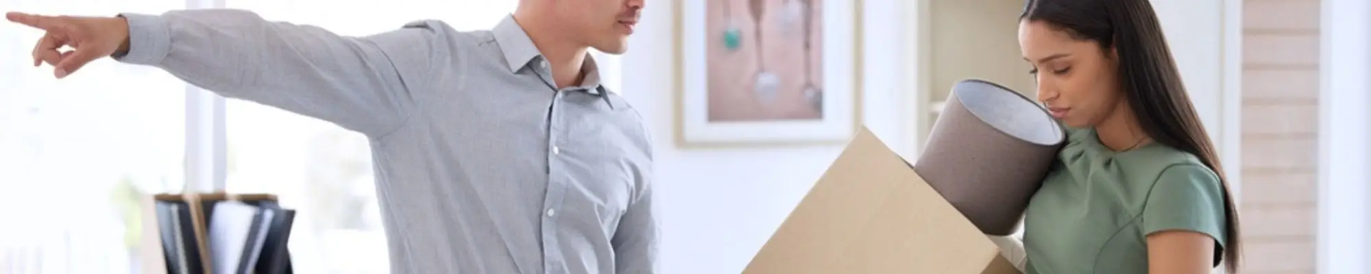 Manager pointing away as a pregnant employee carries a box of belongings